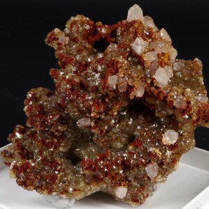 May include: A cluster of pink and white quartz crystals on a matrix of red-brown rock. The crystals are translucent and have a glassy lustre. The rock is rough and textured.