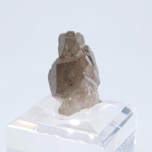 May include: A smoky quartz crystal cluster with a natural, rough texture. The crystal is a light brown color and has a translucent appearance. The crystal is displayed on a clear acrylic base.