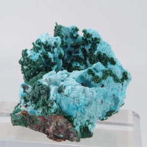 Peut inclure: Spécimen minéral vibrant avec une combinaison de couleurs saisissante. La pièce présente une base de tons bruns riches et terreux, recouverte d'un mélange captivant de turquoise et de vert foncé. La texture semble rugueuse et cristalline.