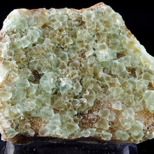 Peut inclure: Un groupe de cristaux de fluorine vert clair sur une matrice brune. Les cristaux sont translucides et ont un éclat vitreux.