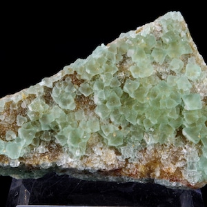 Peut inclure: Un groupe de cristaux de fluorine vert clair sur une matrice brune. Les cristaux sont translucides et ont un éclat vitreux.