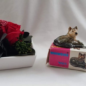 Puede incluir: Una figurita de cerámica de un lobo acostado sobre una caja rosa con la palabra "Whimsies" y la palabra "WOLF" impresa en ella.