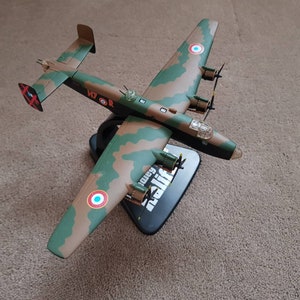 Pode incluir: Um modelo de avião de camuflagem verde, marrom e branco com marcas vermelhas e azuis. O modelo está em um suporte preto com a palavra "Bristol" impressa nele.