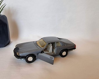May include: A gray toy car with a door open, the interior is visible. The car is on a white surface.