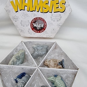 May include: A set of six Wade Whimsy figurines in a hexagonal box. The figurines are made of ceramic and feature various animals, including a beaver, a hippopotamus, a crocodile, a bird, a fish, and a mountain goat. The box is white with the Wade logo and the words "Whimsy" and "English Collectibles" printed on it.