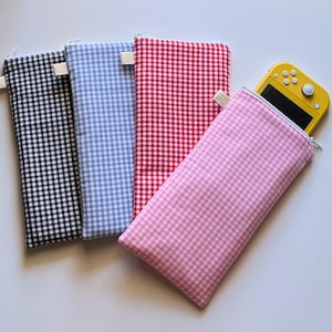 May include: Four gingham-patterned zippered cases in black, light blue, red, and pink. A yellow handheld gaming device is partially visible inside the pink case. Each case has a white fabric loop attached to the zipper.
