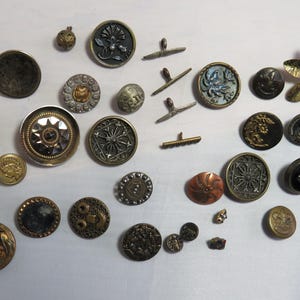May include: A collection of vintage buttons in various colors, shapes, and sizes. The buttons are made of metal and have a variety of designs, including floral, geometric, and abstract patterns.