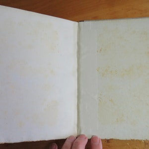 May include: An open book with blank pages. The pages are slightly yellowed with age. The book is bound in a plain, off-white cover.