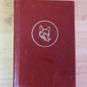 May include: A red leather-bound book with a gold fox head illustration on the cover.