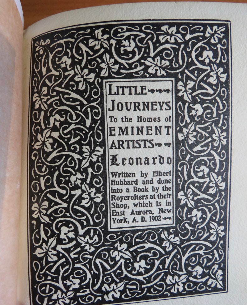 May include: A black and white illustration of a decorative border with a title card that reads "Little Journeys to the Homes of Eminent Artists - Leonardo" and text that reads "Written by Elbert Hubbard and done into a Book by the Roycrofters at their Shop, which is in East Aurora, New York, A. D. 1902."