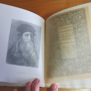 May include: An open book with a black and white illustration of Leonardo da Vinci on the left page. The right page has a decorative border with the text "Little Journeys to the Homes of Great Artists" in the center.