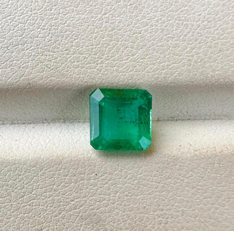 Puede incluir: Una gema de esmeralda verde vibrante cortada en forma cuadrada.