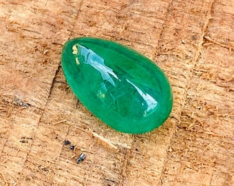 Puede incluir: Una piedra preciosa de esmeralda en forma de lágrima de color verde oscuro. La piedra preciosa es lisa y pulida, con un ligero brillo.