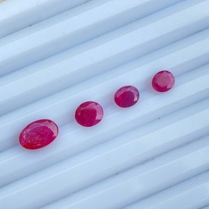 May include: Four oval-shaped, pink gemstones of varying sizes are arranged in a row on a white, textured surface.