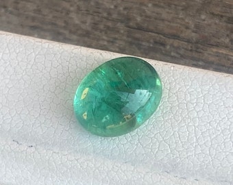 Puede incluir: Una piedra preciosa ovalada de color verde con una apariencia translúcida. La piedra tiene un color verde claro con un toque de amarillo.