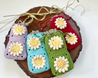 May include: Five crocheted drawstring bags with daisy-shaped designs in shades of purple, blue, green, and red. The bags are arranged on a wooden surface.