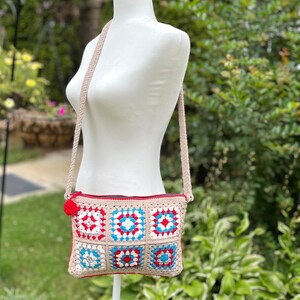 May include: A beige crocheted crossbody bag with a red zipper and a red, white, and blue granny square pattern.