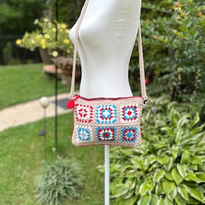 May include: A crocheted crossbody bag with a beige strap and a colorful patchwork design featuring red, blue, and white squares.