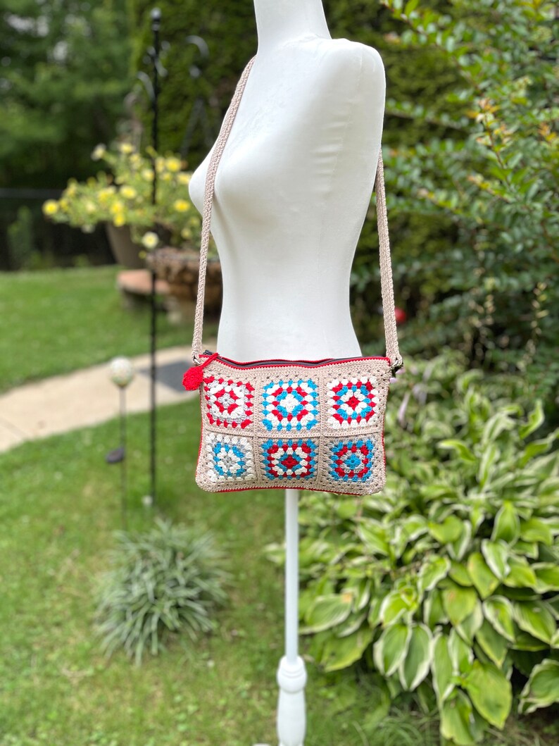 May include: A crocheted crossbody bag with a beige strap and a colorful patchwork design featuring red, blue, and white squares.