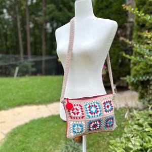 May include: A crocheted crossbody bag with a red, white, and blue geometric pattern. The bag has a zipper closure and a long strap.