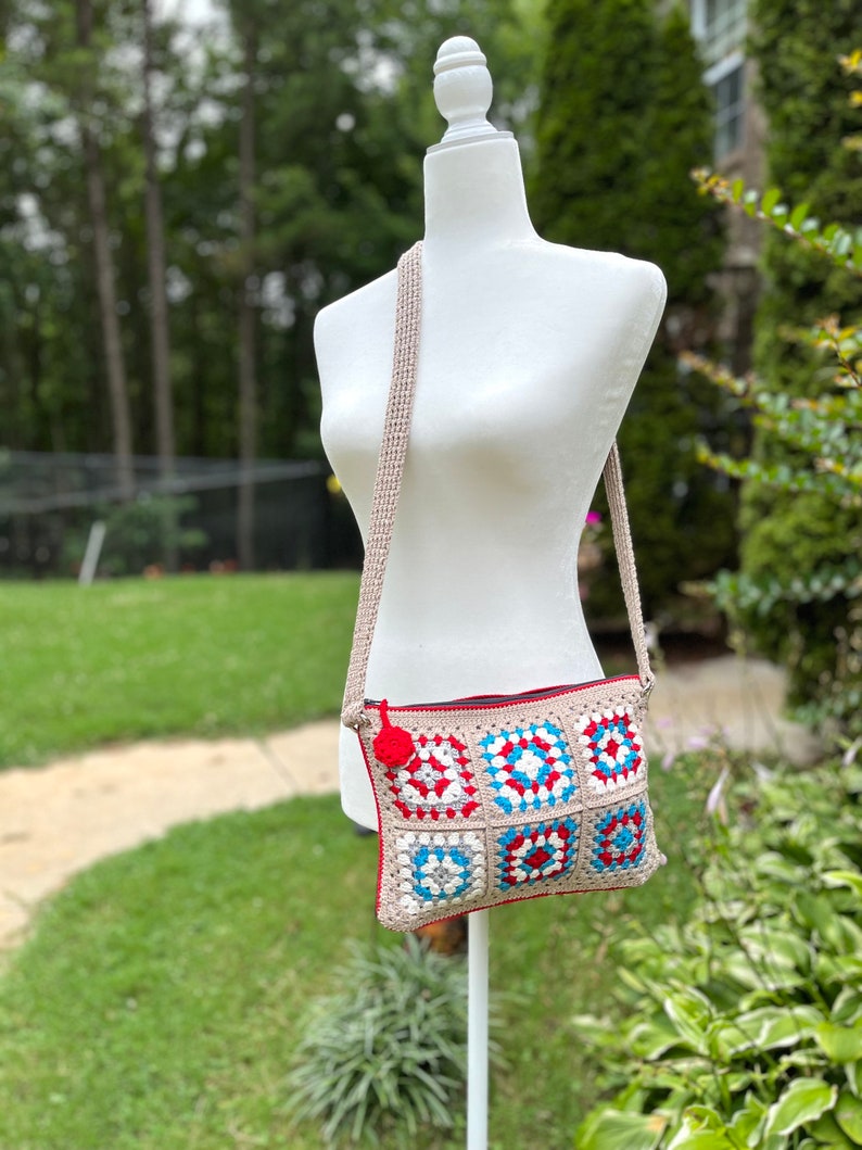 May include: A crocheted crossbody bag with a red, white, and blue geometric pattern. The bag has a zipper closure and a long strap.