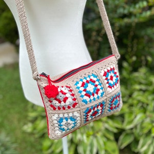 May include: A crocheted crossbody bag with a red, white, and blue geometric pattern. The bag has a zipper closure and a long strap.