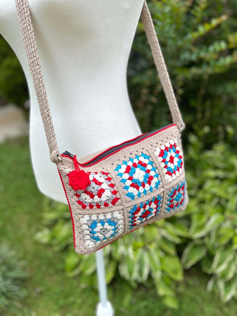 May include: A crocheted crossbody bag with a red, white, and blue geometric pattern. The bag has a zipper closure and a long strap.