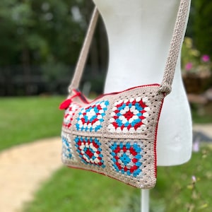 May include: A crocheted crossbody bag with a beige strap and a colorful geometric pattern in red, white, blue, and gray.
