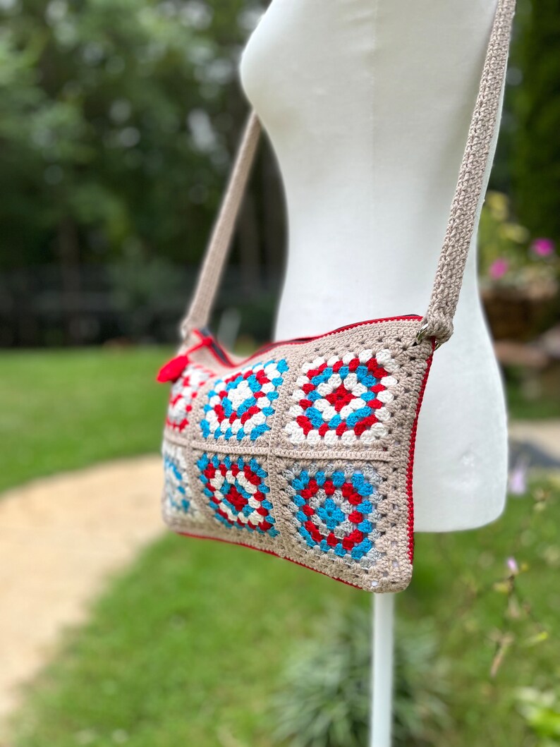 May include: A crocheted crossbody bag with a beige strap and a colorful geometric pattern in red, white, blue, and gray.
