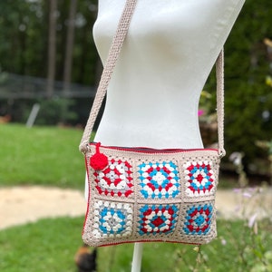 May include: A crocheted crossbody bag with a red, white, and blue granny square pattern. The bag has a beige strap and a red zipper.