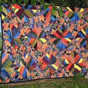 May include: A quilt with a patchwork design featuring a variety of colors and patterns, including blue, green, red, and yellow. The quilt is made of fabric with a leaf print and is bordered with a black trim.