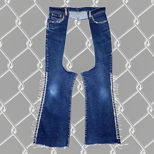 May include: A pair of dark blue denim jeans with a cut-out in the back and white fringe along the sides. The jeans have a high waist and a straight leg.