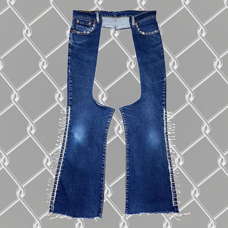 May include: A pair of dark blue denim jeans with a cut-out in the back and white fringe along the sides. The jeans have a high waist and a straight leg.
