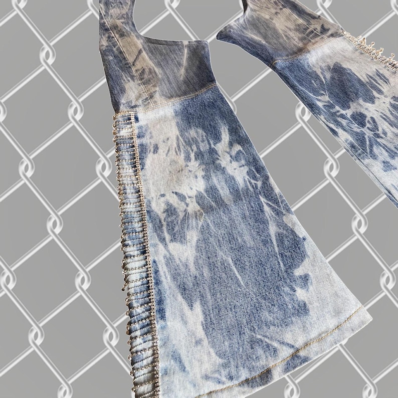 May include: A pair of blue denim jeans with a tie-dye pattern and a beaded trim along the sides.