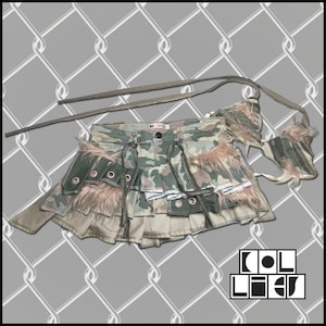 May include: A camouflage denim mini skirt with multiple layers and decorative straps. The skirt features faux fur accents and a matching strap. The skirt has a button closure and a brand label. The skirt is a unique fashion item.