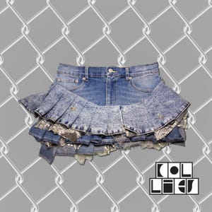 May include: A denim skirt with a layered design. The skirt features a pleated, acid-wash denim layer over a layer of silver and patterned fabric. The skirt has a button and zipper closure. The brand name "COL LIEU" is in the bottom right corner.