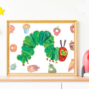 May include: A framed print featuring a colorful illustration of a green caterpillar with a red head, surrounded by images of food items. The artwork is in a wooden frame and is displayed on a wooden shelf with a red toy rocket.