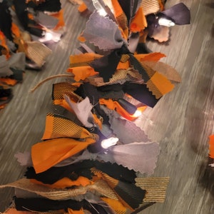 May include: A Halloween garland made of orange, black, and gray fabric scraps with white lights woven throughout.