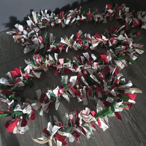 May include: A Christmas garland made of fabric scraps in red, green, white, and brown. The garland is made of strips of fabric that are tied together and then frayed to create a fluffy look.