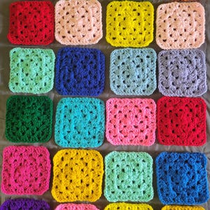 May include: A collection of twenty-four square crochet motifs arranged in a grid. Each square features a classic granny square pattern with a central cluster and radiating stitches in various solid colors including purple, yellow, green, orange, red, pink, and blue.