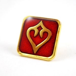 Peut inclure: Une broche carrée dorée avec un fond en émail rouge. La broche présente un motif de cœur stylisé en or.