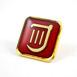May include: A gold-coloured pin with a red background featuring a stylised harp design.