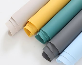 Könnte beinhalten: Fünf aufgerollte Silikon-Tischsets in verschiedenen Farben: Beige, Gelb, Türkis, Grau und Hellblau.