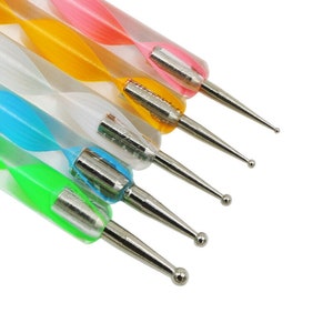 Könnte beinhalten: Satz mit fünf Nagelkunstwerkzeugen mit verschiedenen Spitzenformen. Die Werkzeuge haben bunte, gestreifte Griffe.