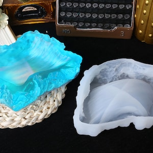 Könnte beinhalten: Zwei Silikonformen zum Gießen von Harz. Eine Form ist hellblau und die andere weiß. Beide Formen sind wellenförmig.