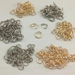 Può includere: Un assortimento di anelli di salto in metallo nei toni oro, argento e bronzo. Gli anelli di salto sono di varie dimensioni e vengono utilizzati per la creazione di gioielli e l'artigianato. L'immagine mostra una varietà di anelli aperti e chiusi.