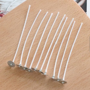 May include: A set of 15 white candle wicks with metal bases. The wicks are arranged in a fan shape on a wooden surface.