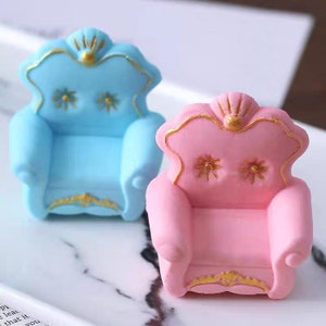 Könnte beinhalten: Zwei Miniatur-Sessel aus Keramik. Einer ist hellblau mit goldenen Verzierungen, der andere ist rosa mit goldenen Verzierungen.