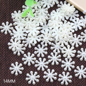 Könnte beinhalten: Nahaufnahme einer großen Menge weißer Perlen-Schneeflocken-Verzierungen. Die Schneeflocken sind etwa 14 mm groß und aus weißen Kunststoffperlen gefertigt.