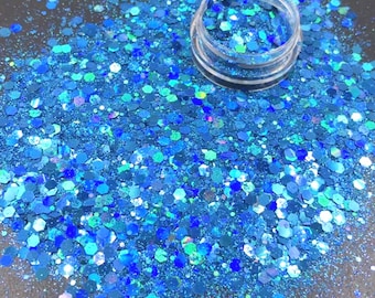 May include: A close-up of a jar filled with blue and teal iridescent glitter. The glitter is scattered around the jar on a black surface.